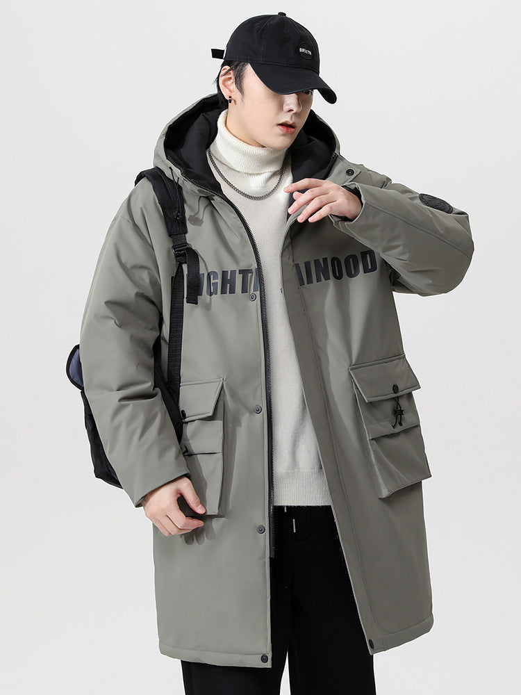 A man wearing olive NEIGHBORHOOD parka with black hood carries a backpack while standing against white background in complete outfit
