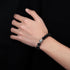  A person wearing a black beaded bracelet with a marbled gray accent bead, hand resting on the chest.