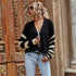 A woman in sunglasses poses wearing a black button-up cardigan with cream striped sleeves, white top, and light wash jeans against architectural backdrop