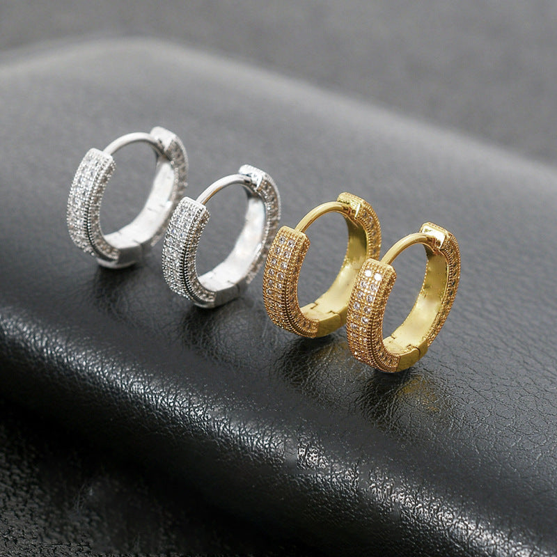 Two pairs of luxury huggie hoop earrings with cubic zirconia crystals, one pair in silver tone and one in gold tone, displayed on black leather surface