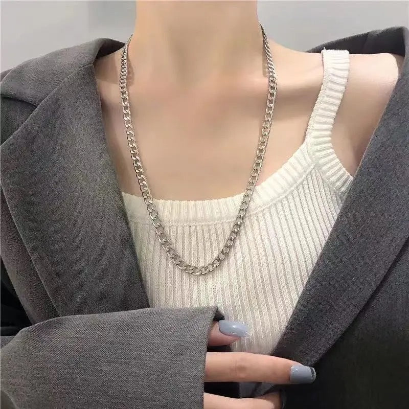 Silver curb chain necklace worn with white ribbed top and grey blazer, showing grey manicured nails