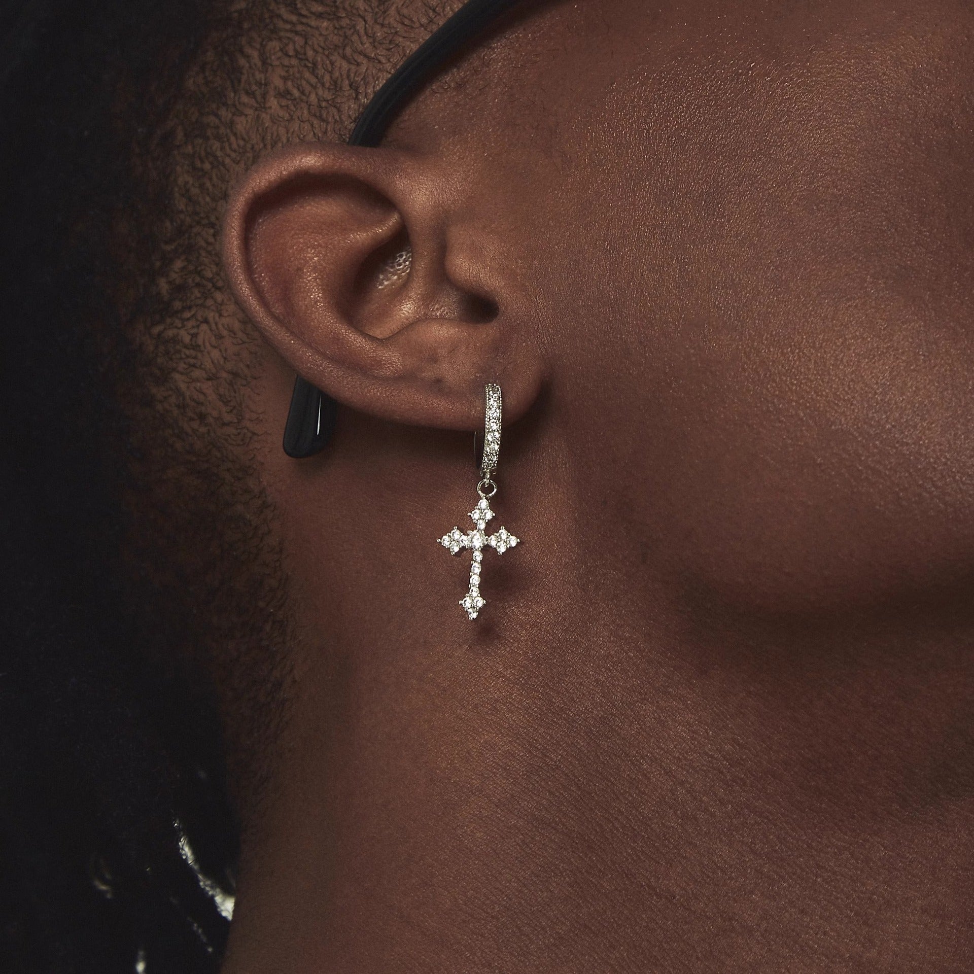 Zircon cross drop earring worn on dark skin, with black stud visible above