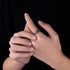 A person wearing a silver skull and crossbones ring, gently touching their fingers together, showcasing the ring’s bold style.
