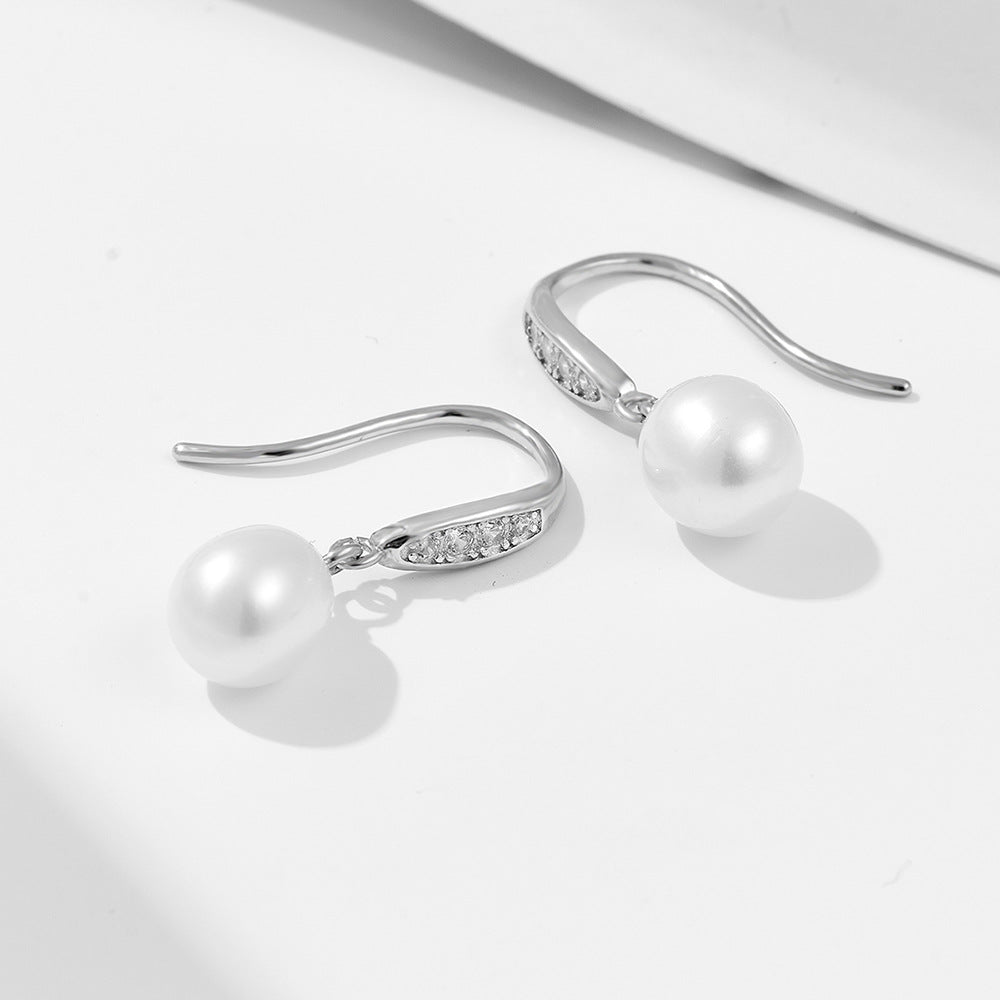 Side view of silver earrings with pearls and crystal details against white background