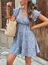 Woman posing with a woven bag, wearing a baby blue ruffle sleeve babydoll dress with a V-neck and tiered design.