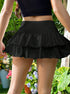 Detail view of black tiered ruffle mini skirt showing flowing fabric movement against floral garden background