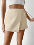 Side view of cream wrap skort featuring textured fabric and adjustable tie detail, paired with delicate gold bracelet