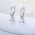Silver huggie hoop earrings with double diamond drop charms, displayed on white surface with '925' stamp visible