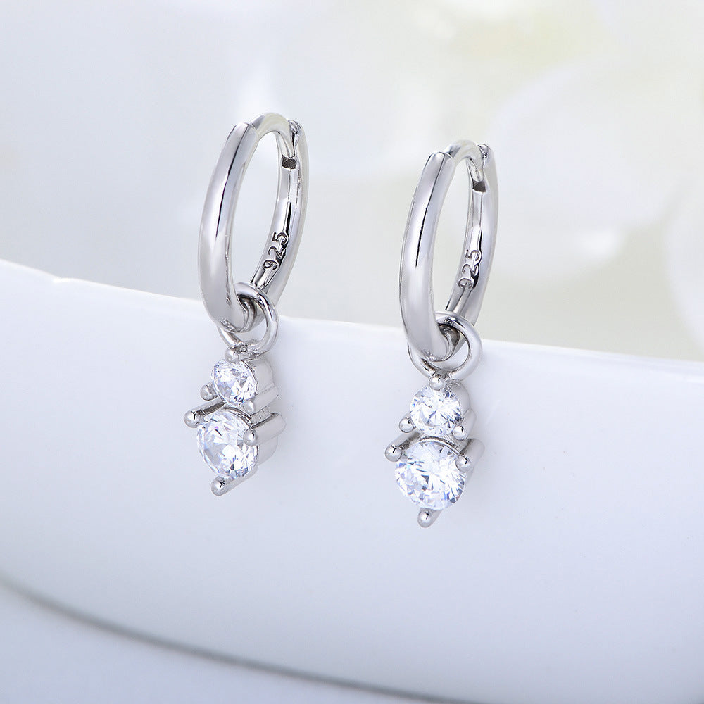 Silver huggie hoop earrings with double diamond drop charms, displayed on white surface with '925' stamp visible