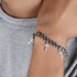  Close-up of a silver bracelet with multiple cross charms, styled with a casual gray shirt for a trendy look.
