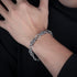 A man’s hand resting on his chest, wearing a silver rope-link bracelet with interwoven details, paired with a black shirt.