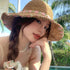 Woman wearing a brown woven straw hat with pink floral embroidery, posing by a poolside with palm trees in the background.