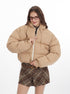 Woman wearing a beige puffer jacket with a plaid mini skirt, smiling and posing against a white background