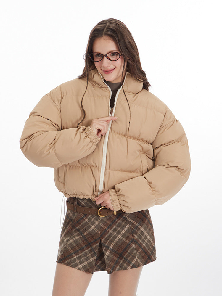 Woman wearing a beige puffer jacket with a plaid mini skirt, smiling and posing against a white background