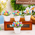 Four white flower pots, each holding a bouquet of artificial speckled Easter eggs in pastel and vibrant shades, displayed on a wooden box with floral decor.