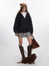 A model in a black hoodie, white shirt, and gray skirt walks a brown dachshund on a leash while holding a brown suede handbag