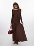 Side view of brown jersey maxi dress highlighting dropped waist silhouette, ruched bodice detail, and attached neck scarf, paired with burgundy accessories