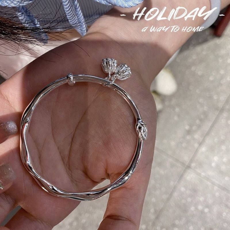 A person is holding a silver twisted bangle bracelet with crown-shaped charm details on their palm, with 'HOLIDAY' promotional text overlay
