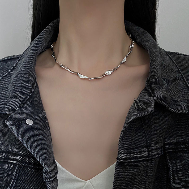 Woman wearing a silver sculpted chain necklace with an organic, wavy design, paired with a denim jacket