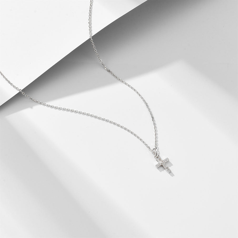 Silver cross pendant necklace with diamond pavé accents on fine link chain, photographed against geometric white background