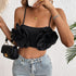 Woman in a black floral crop top and jeans, accessorizing with gold jewelry and holding a black quilted handbag.