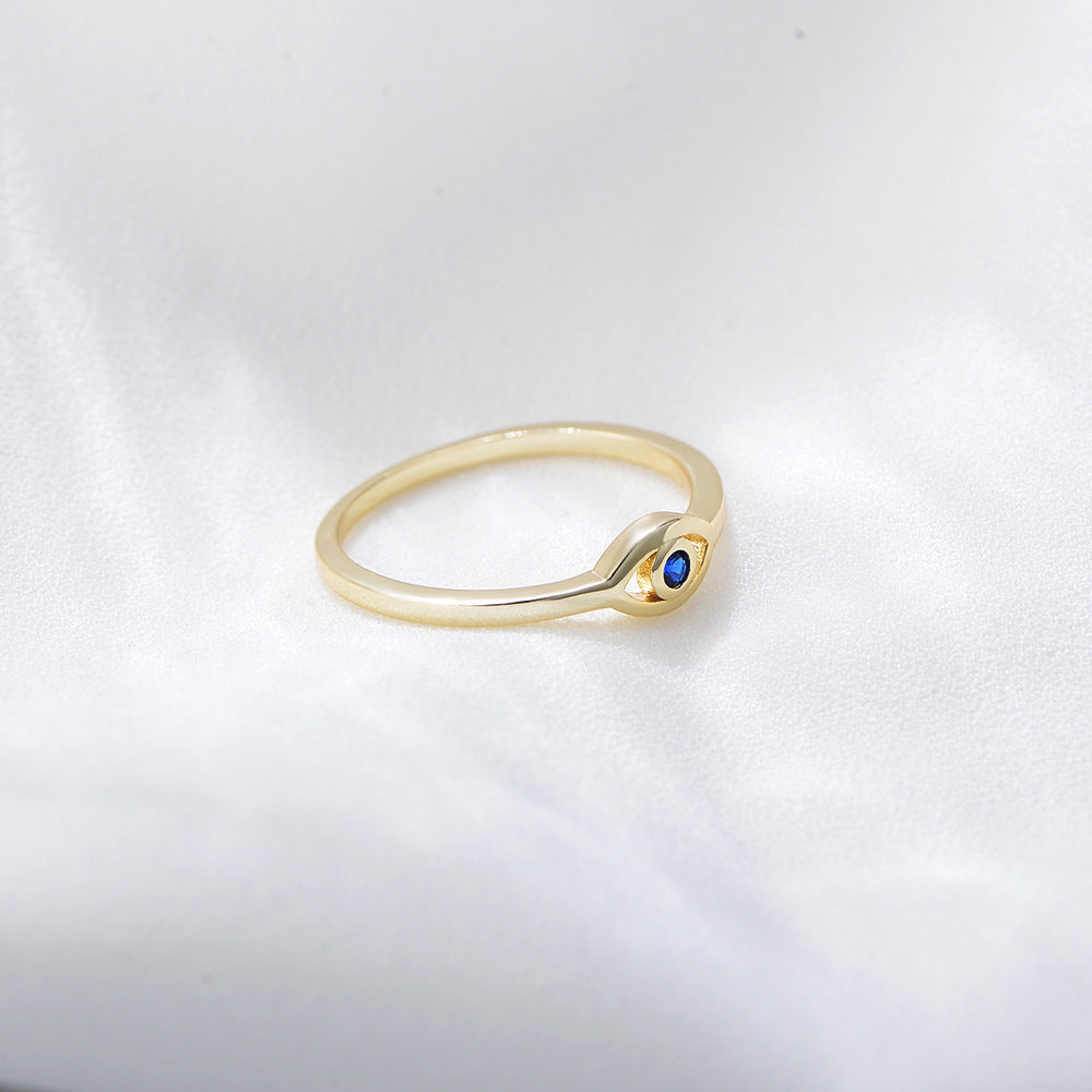 Side view of gold ring featuring eye-shaped design with blue sapphire on white surface