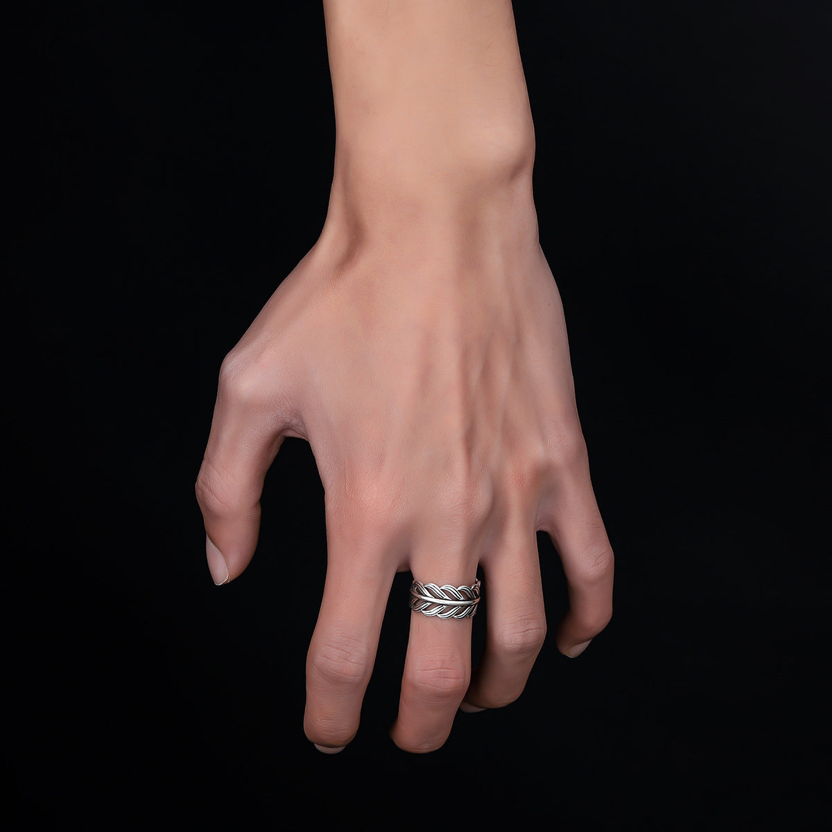 A detailed shot of a silver feather-shaped adjustable ring placed on a reflective black surface, illuminated by a spotlight.