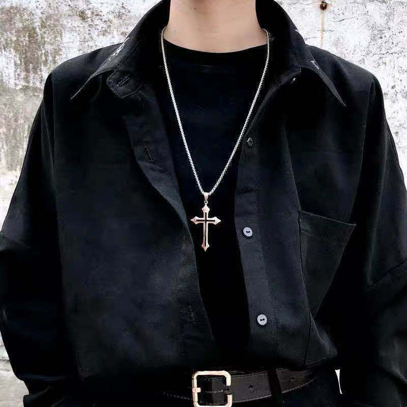 Man wearing a silver cross pendant necklace over an all-black outfit, styled with a button-up shirt