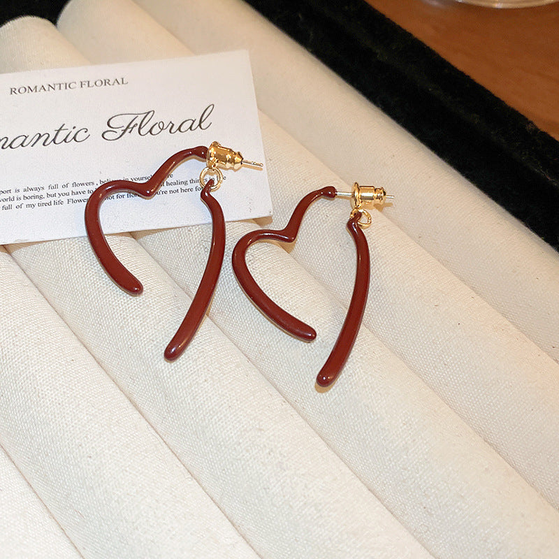 A pair of asymmetrical heart-shaped red enamel earrings with gold posts is displayed on a jewelry tray with a "Romantic Floral" card