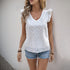 Woman in a white embroidered V-neck top with ruffle sleeves, styled with denim shorts and layered jewelry, posing against a neutral wall.