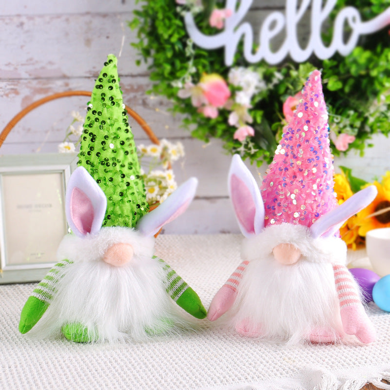 Two plush bunny gnome decorations with green and pink sequin hats, placed on a textured white table.
