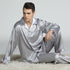 Model sitting on white fluffy rug wearing silver silk pajamas with diamond pattern and chest pocket