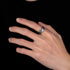A close-up of a hand wearing a rugged silver ring with an uneven surface, displayed elegantly against a black background.