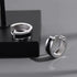 Silver huggie hoop earrings with black inlay, displayed on black platform with dramatic shadows