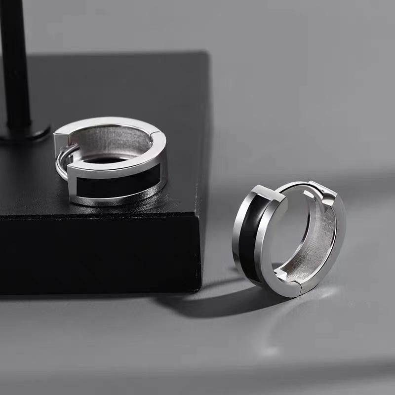 Silver huggie hoop earrings with black inlay, displayed on black platform with dramatic shadows