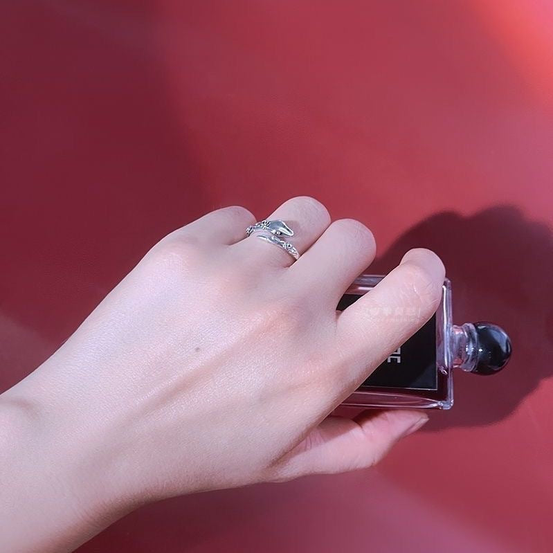 A model is holding a perfume bottle while wearing a silver snake ring. Red background highlights the adjustable band