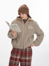 Model reading poetry book while wearing beige teddy fleece jacket with Marule patch, brown beanie and plaid pants on white background
