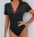 Close-up of a woman wearing a black bodysuit with lace details at the neckline and short sleeves, accessorized with gold layered necklaces.