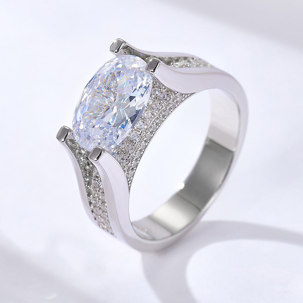 A silver engagement ring featuring oval-cut diamond in four-prong setting with diamond-encrusted band on white surface