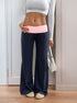 Front view of navy blue wide-leg pants with a pink fold-over waistband, paired with a white cropped long-sleeve top and beige slippers.