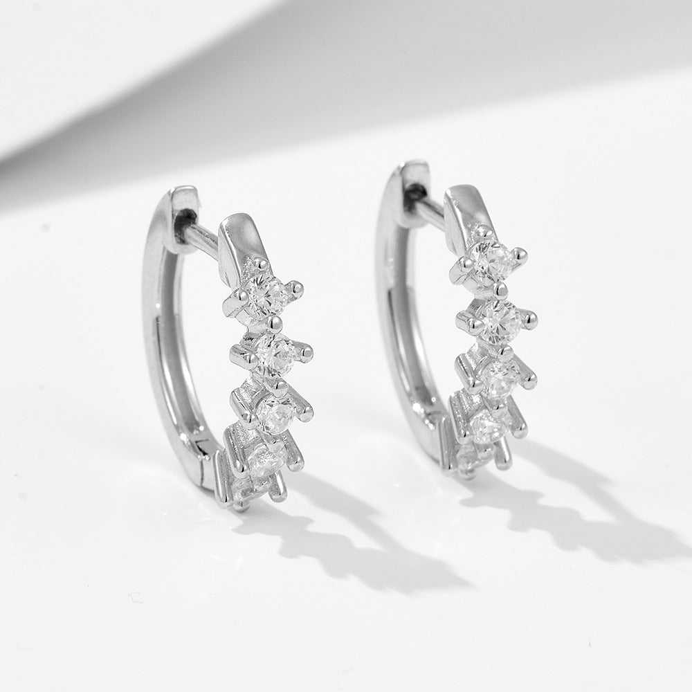 Close-up of silver huggie hoops with five prong-set crystals casting dramatic shadows