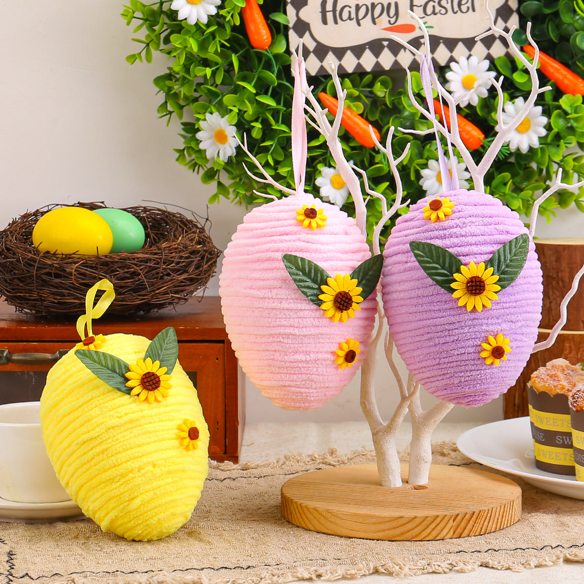 Three Easter egg decorations in pink, purple, and yellow hanging from a white tree stand, each measuring 13cm x 10cm.