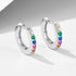 A pair of silver huggie hoop earrings with colorful rainbow gemstones arranged in sequence on minimalist backdrop