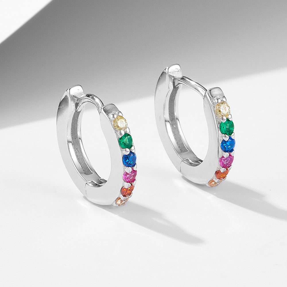 A pair of silver huggie hoop earrings with colorful rainbow gemstones arranged in sequence on minimalist backdrop