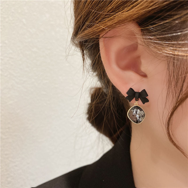 Close-up of an ear wearing a black bow earring with a dangling cushion-cut gray crystal in gold setting