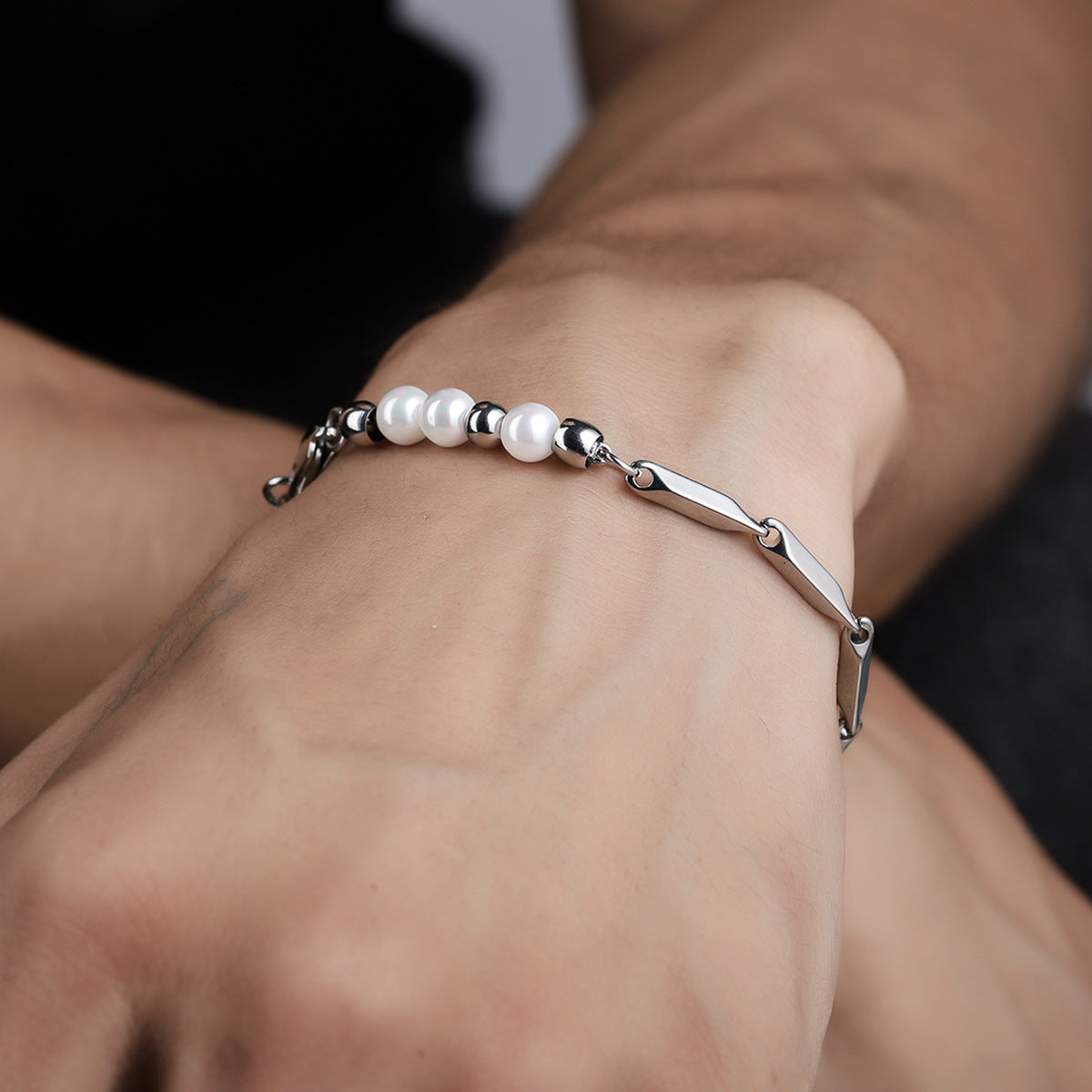 Men's stainless steel bracelet with white pearls and geometric links, worn on wrist. Elegant and modern design for everyday wear.