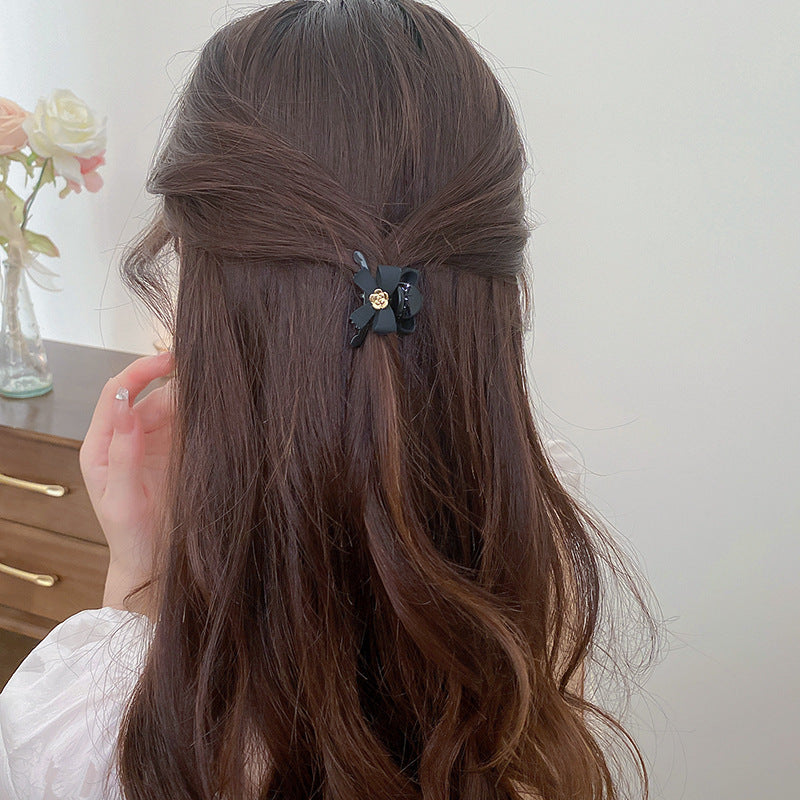 Black bow hair clip with gold flower center worn in half-up hairstyle