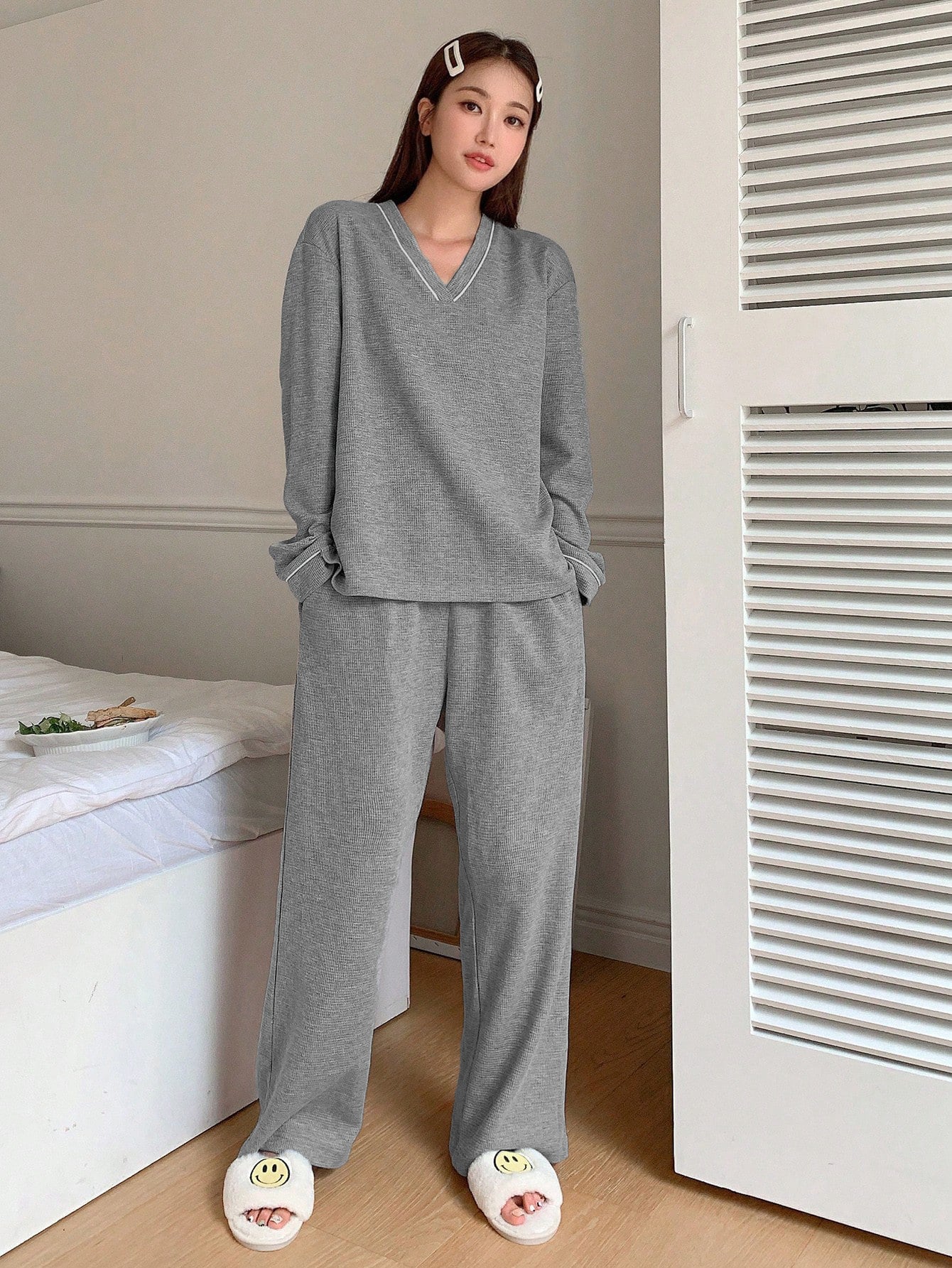 Full-length view of gray V-neck pajama set with white piping detail and fuzzy smiley face slippers