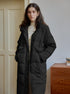 Black maxi puffer coat with high collar and utility pockets, styled with cream turtleneck, minimalist interior setting