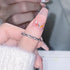 Finger wearing twisted diamond band ring with pink manicure featuring colorful gemstone nail art embellishments